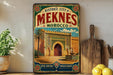 a vintage-style poster of the historic city of Meknes, Morocco, with a detailed illustration of the city's architecture and a palm tree. The poster is displayed on a wall, surrounded by various kitchen utensils and a potted plant.