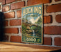 A vintage-style metal sign with the text "HOCKING STATE FOREST OHIO" is displayed on a brick wall.