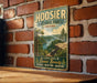 A vintage-style metal sign for Hoosier National Forest, Indiana, featuring a scenic landscape with a river and mountains.