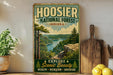 A vintage-style sign for Hoosier National Forest in Indiana, featuring a scenic landscape with a river and forest.