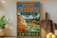 A vintage-style sign for Hot Springs State Park in Wyoming, featuring a scenic illustration of the park's natural beauty.
