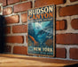 A vintage-style metal sign for Hudson Canyon National Marine Sanctuary, featuring an illustration of underwater marine life and the text "Hudson Canyon National Marine Sanctuary" and "New York".