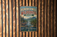 A vintage-style metal sign with the text " Hundred Mile Wilderness Maine" and a scenic illustration of a forest, mountains, and moose.