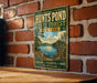 A vintage-style metal sign for "Hunts Pond State Forest New York" is displayed on a brick wall, featuring a scenic landscape with a lake and pine trees.