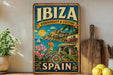 A vintage-style metal sign with a colorful illustration of a coastal town in Ibiza, Spain, featuring a castle, palm trees, and a sailboat.