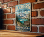 A vintage metal sign for the Glacier National Park in Montana, featuring a scenic mountain landscape with a lake in the background.