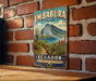 A vintage-style metal sign for Imbabura Park in Ecuador, featuring a scenic landscape with mountains, a lake, and a path leading through the greenery.