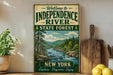 A vintage-style sign welcoming visitors to Independence River State Forest in New York, featuring a scenic illustration of a river surrounded by pine trees and mountains.
