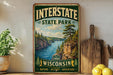 A vintage-style sign for Interstate State Park in Wisconsin, featuring a scenic landscape with a river and mountains.
