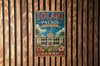 A vintage metal sign for the Iolani Palace in Hawaii, featuring a tropical illustration of the palace surrounded by palm trees and flowers.