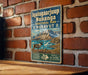 A vintage-style metal sign with text and an illustration of a reindeer in a mountainous landscape, mounted on a brick wall.