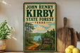 A vintage-style sign for John Henry Kirby State Forest in Texas, featuring a scenic landscape with a lake and pine trees.