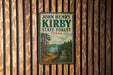 A vintage-style metal sign for John Henry Kirby State Forest in Texas, featuring a scenic illustration of a forest and a lake.