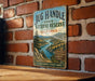 A vintage-style metal sign for the Jug Handle State Natural Reserve in California, featuring a scenic landscape with mountains, trees, and a river.