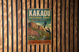 A vintage-style metal sign for Kakadu National Park in Australia, featuring an illustration of a bird and a landscape with a lake and mountains.