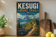 A vintage-style sign for the Kesugi Ridge Trail in Alaska, featuring a scenic mountain landscape with a winding trail.