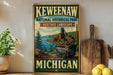 A vintage-style sign for Keweenaw National Historical Park, featuring a scenic landscape with a train and a river, is displayed on a shelf next to a wooden cutting board and some lemons.