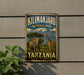 A metal sign displaying the name "Kilimanjaro National Park Tanzania" with an illustration of an elephant and a giraffe in a natural setting.
