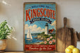 A vintage-style metal sign welcoming visitors to Kingscombe, Rhode Island, featuring a lighthouse, sailboat, and coastal scenery.