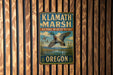 A metal sign with the text "Klamath Marsh National Wildlife Refuge Oregon" is displayed on a wooden fence.