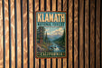 A vintage-style metal sign for Klath National Forest in California, featuring a scenic landscape with a mountain, river, and pine trees.
