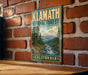 A vintage-style metal sign for Klath National Forest in California, featuring a scenic mountain landscape with pine trees and a river flowing through the forest.