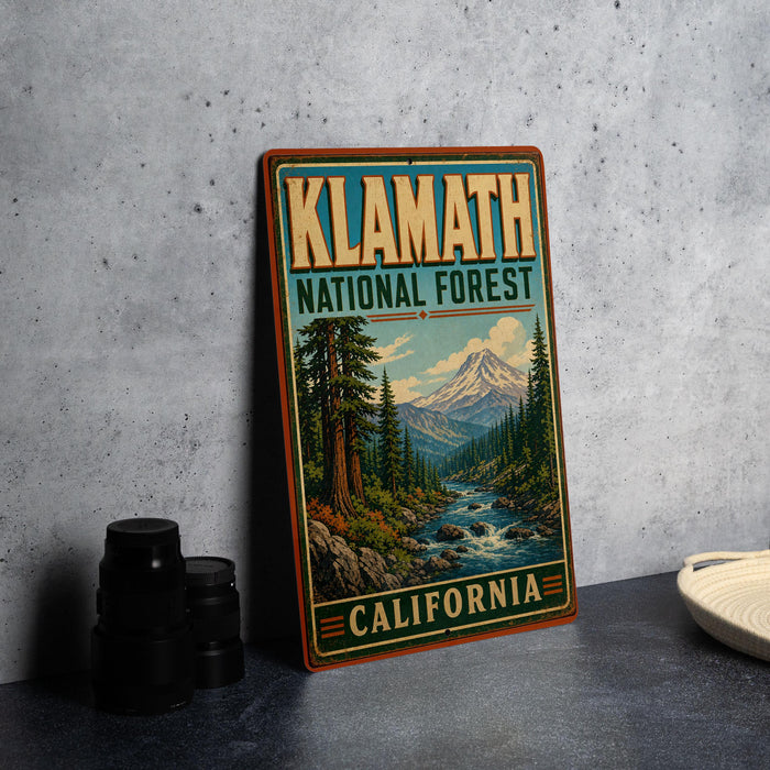 A vintage-style sign for Klamath National Forest in California, featuring a scenic illustration of a forest landscape with a mountain in the background.