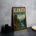 A vintage-style sign for Klamath National Forest in California, featuring a scenic illustration of a forest landscape with a mountain in the background.