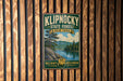 A vintage-style metal sign for Klipnocky State Forest in New York, featuring a scenic landscape with pine trees, a lake, and mountains.