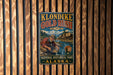 A vintage-style metal sign for Klondike Gold Rush National Historical Park in Alaska, featuring an illustration of a man panning for gold in a river.