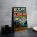 A vintage-style sign advertising Kluane, Wrangell-St. Elias, Glacier Bay, and Tsathershini-Alesk, with a moose and mountains in the background.