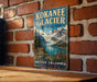 A vintage-style metal sign for the Kokanee Glacier in British Columbia, Canada, featuring a scenic mountain landscape with a lake and wildflowers.