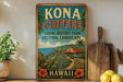 A vintage-style metal sign for Kona Coffee, featuring a tropical landscape with a house, palm trees, and coffee plants, is displayed on a shelf next to a wooden cutting board and some lemons.