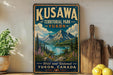 A vintage-style metal sign for Kuskawa Territorial Park in Yukon, Canada, featuring a scenic mountain landscape with a lake and pine trees.