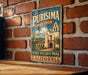 A vintage metal sign with the text "La Purismo Mission State Historic Park California" is displayed on a brick wall.
