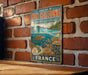 A vintage metal sign for the Lagoon of New Caledonia, featuring an illustration of a coral reef and marine life, is displayed on a brick wall.