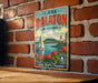 A vintage-style metal sign with the text "Lake Balaton, Hungary" and a sailing ship illustration, mounted on a brick wall.
