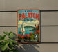 A vintage-style metal sign with the text "LAKE BALATON HUNGARY" and a sailboat image, hanging on a wall.