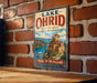 A vintage-style sign for Lake Ohrid in North Macedonia, featuring a castle and a boat on the water.