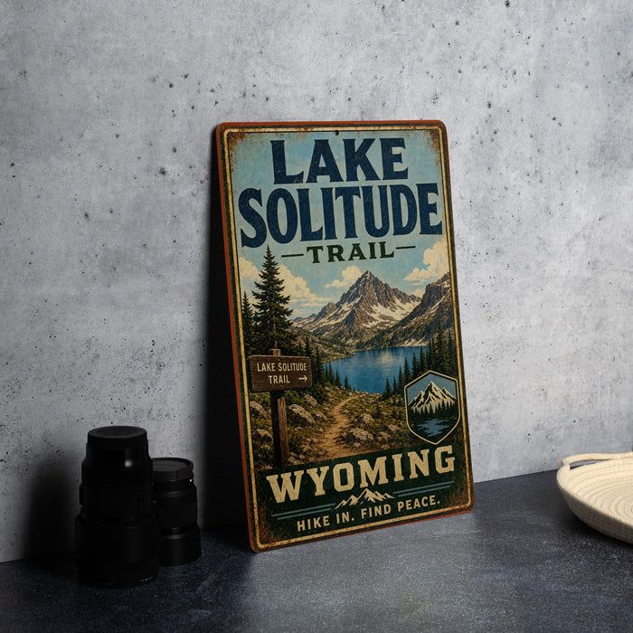 A vintage-style sign for the Lake Solitude Trail in Wyoming, featuring a scenic mountain landscape and a trail sign.