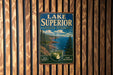 A vintage metal sign for Lake Superior State Forest, featuring a scenic landscape with pine trees, cliffs, and a body of water.