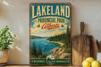 A vintage-style sign for Lakeland Provincial Park, Alberta, featuring a scenic landscape with pine trees, a lake, and mountains.