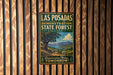 A vintage metal sign for the Las Posadas State Forest in California, featuring a scenic landscape with a large tree and mountains in the background.