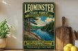 A vintage-style metal sign for Leominster State Forest in Massachusetts, featuring a scenic image of a forest and a lake.