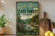 A vintage-style metal sign for Little River State Forest in Alabama, featuring a scenic image of a river surrounded by trees and mountains.