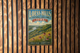 A vintage-style metal sign for Loess Hills, Iowa, featuring a scenic landscape with a river and flowers.