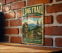 A vintage-style metal sign for the Long Trail in Vermont, featuring a scenic mountain landscape and trail marker.