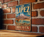 A vintage-style metal sign with the text "LOS LÍPZ" and "BOLIVIA" displayed prominently, featuring an illustration of a llama and a mountain landscape.