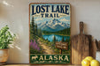 a vintage-style sign for the Lost Lake Trail in Alaska, with a scenic mountain landscape and a path leading to a lake.
