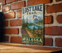 a vintage-style sign for the Lost Lake Trail in Alaska, mounted on a brick wall.